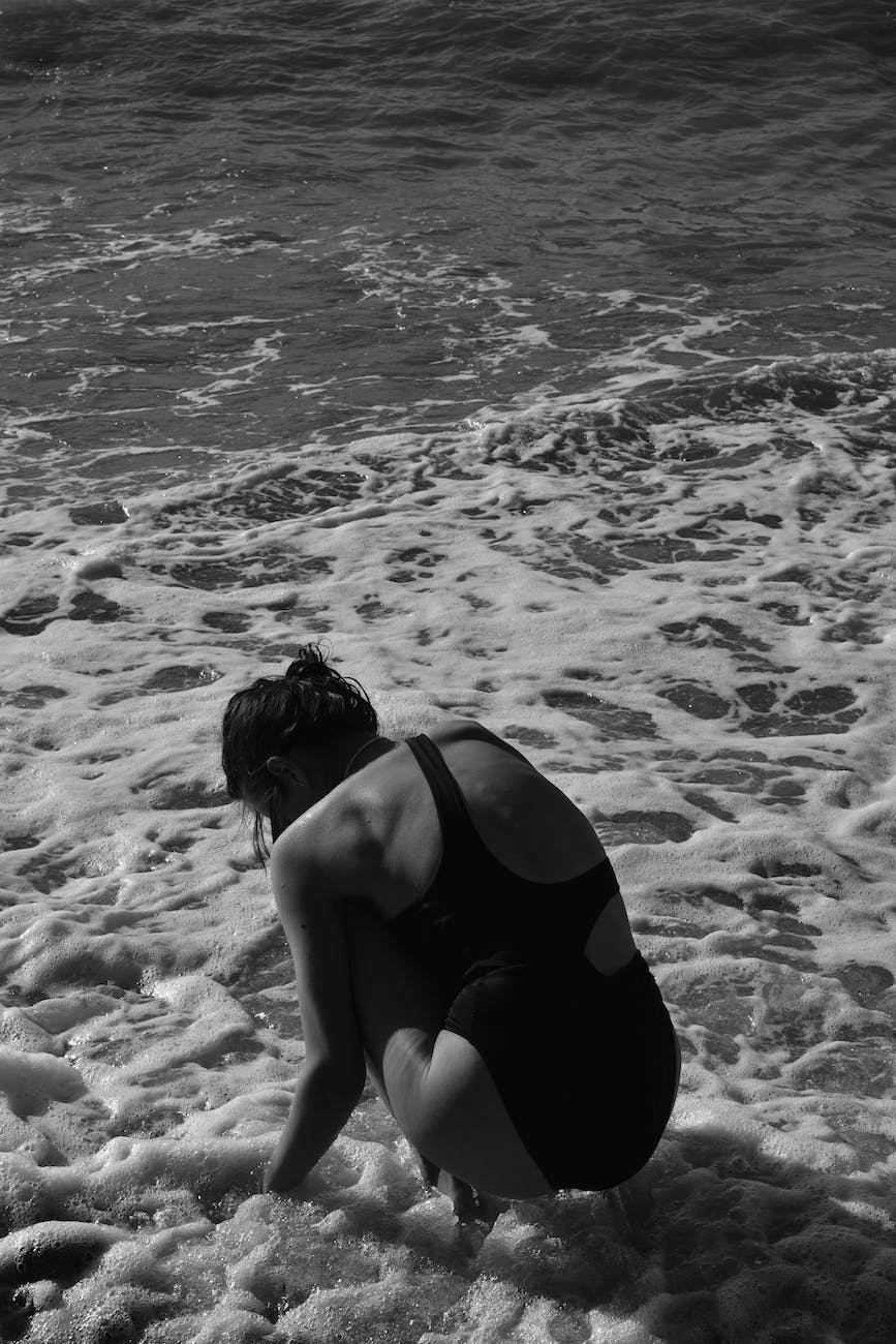 young woman in a swimsuit crouching ankles deep in water